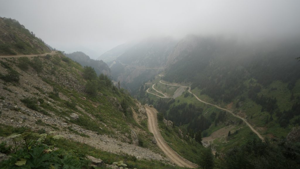 View of the street from above in the fog. It runs through a mountainous landscape and contains many curves.