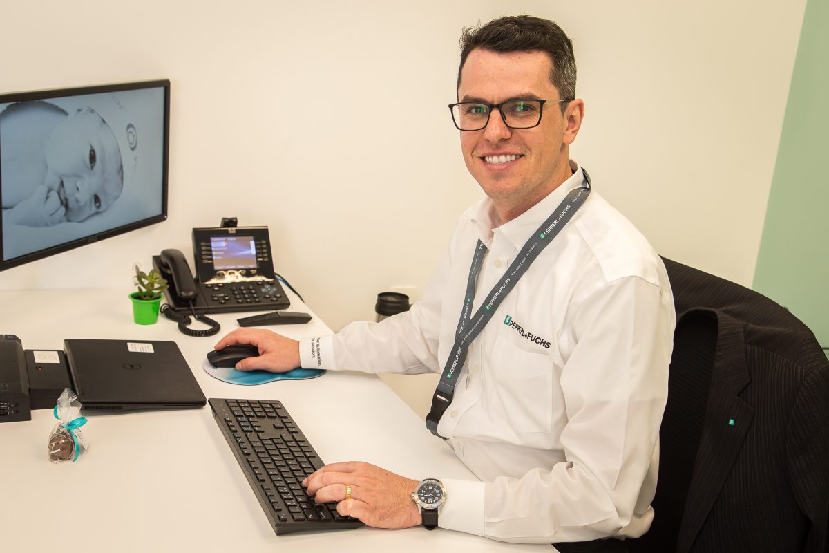 Dênis, Regional Sales Director FA at Pepperl+Fuchs in Brazil sits at his desk in the office and smiles into the camera.