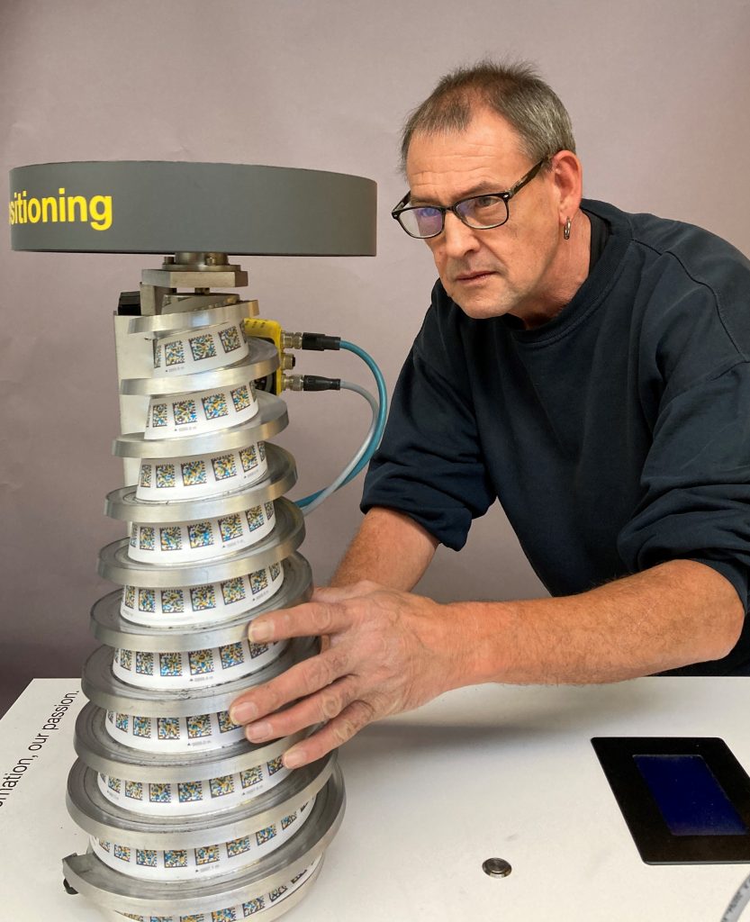 Bernd is celebrating his 40 years of service and has already built many exhibits for Pepperl+Fuchs. Here he is currently constructing an exhibit. You can see a spiral that gets smaller towards the top, with lots of QR codes on it.