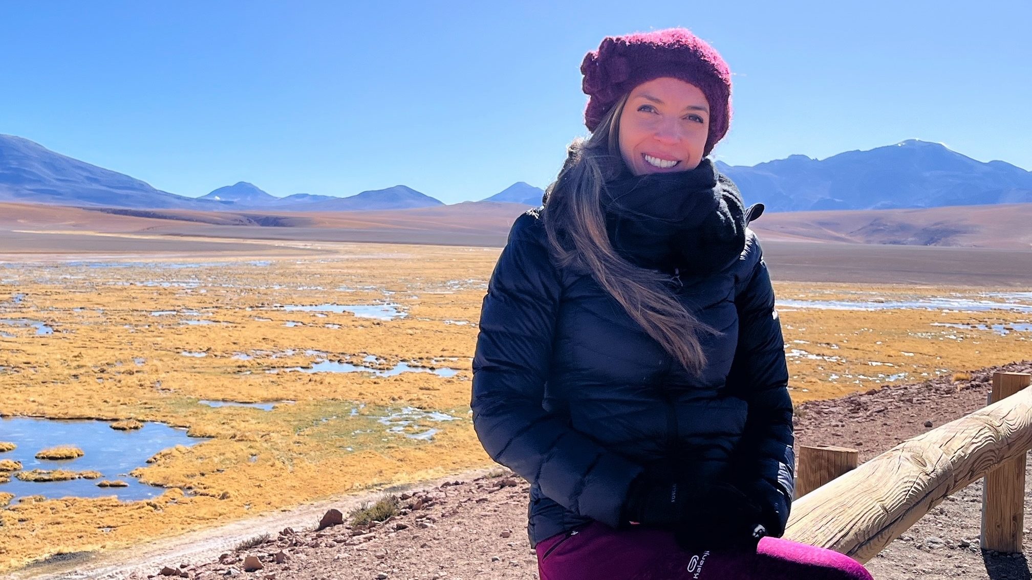 In this picture you can see Carina in the Atacama Desert in Chile. She sits on a wooden barrier and smiles into the camera.