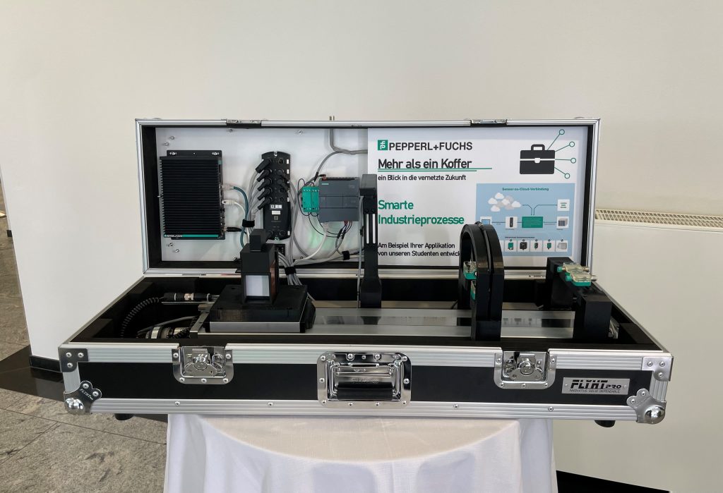 Close-up of the suitcase exhibit: The linear axis and various Pepperl+Fuchs sensors are clearly visible. The exhibit sits on a round table covered with a white tablecloth.