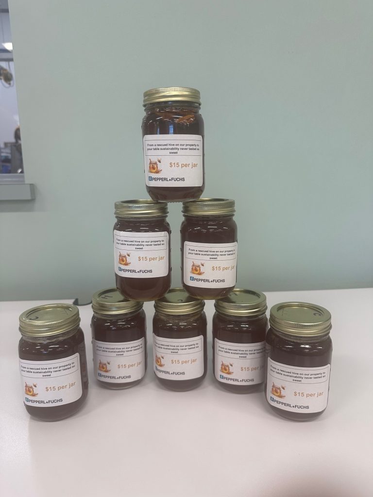 Nine jars filled with honey are arranged in the shape of a pyramid on a table.